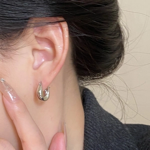 Macro shot of a silver polished U-shaped geometric earring worn on model's earlobe