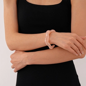 Detail view of pink irregular acrylic bangle worn by a model in black vest clothing