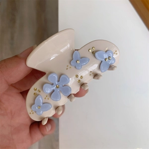 Detailed close-up of beige acetate hair claw clip with blue flowers and gold beads