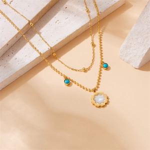 Detail of layered gold necklace with turquoise beads and white star pendant on stones