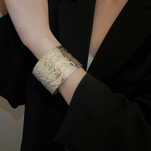 Detailed view of wide gold cuff bracelet featuring hammered lava texture on a black suit