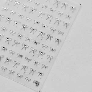 Nahaufnahme von 3D-Nagelstickern mit silbernen Schleifen und funkelnden Diamantelementen