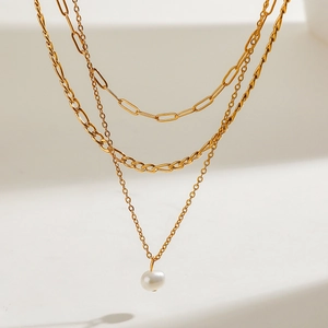 Three-layer gold stainless steel necklace with elegant white pearl pendant on beige background