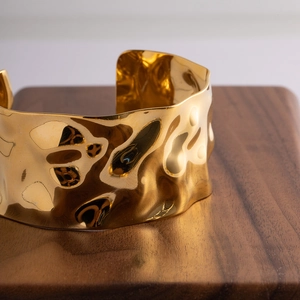 Macro view of 18K gold hammered wide cuff bracelet on a walnut wood display stand