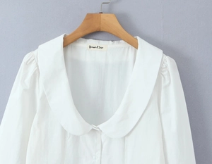 Detailed view of a white long-sleeve blouse featuring a Peter Pan collar on a wooden hanger