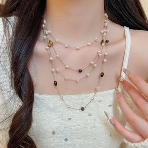 Dettaglio di una collana multistrato con perle occhio di tigre e perle bianche su una modella