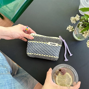 Close-up of a colorful woven makeup pouch with Sozakka brand tag in a cafe setting