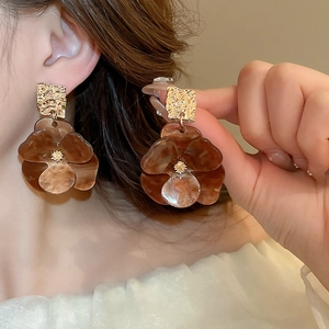 Detail of amber acrylic flower earring with textured gold square stud on model