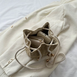 Beige woven straw bucket bag with drawstring closure showing internal storage and phone