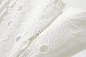 Gros plan détaillé sur la broderie blanche et la fermeture éclair invisible de la robe