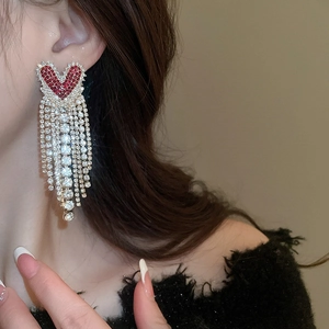 Macro detail of sparkling red heart stud and long silver tassel fringe earrings