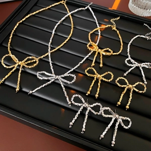 Exquisite gold and silver bow necklaces and earrings displayed on a black jewelry tray