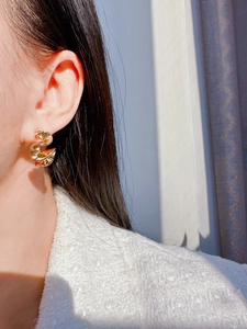 Detailed view of twisted liquid metal gold earrings on model with white tweed background