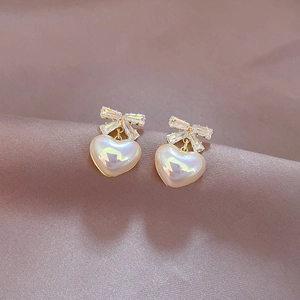 Macro shot of gold bow stud earrings with heart charms on soft purple silk