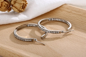 Detailed view of silver hoop earrings with white zircon inlay on a wooden tray