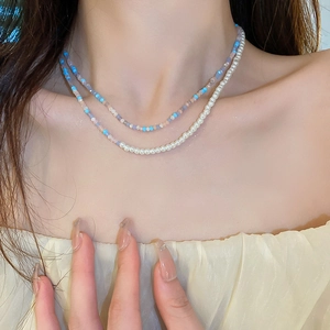 Close-up of double-layered beaded necklace with blue pink stones and white pearls on model neck