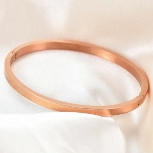 Detail of a minimalist rose gold stainless steel bangle on elegant silk fabric