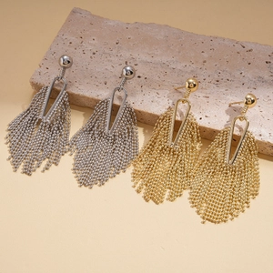 Hollow geometric earrings with tassels in gold and silver finish on stone background