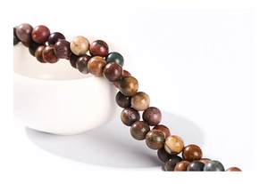 Close-up of multicolored natural picasso stone round beads on a white porcelain bowl