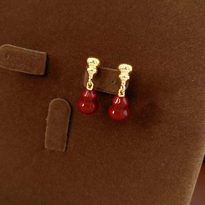 Detailed shot of 18k gold plated red gourd earrings on a brown velvet jewelry display