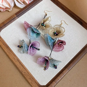 Detail of fabric flower earrings with mesh petals and gold beads on a wooden grid tray