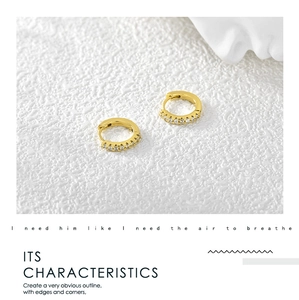 Detail of gold huggie earrings with cubic zirconia inlay on a white textured background