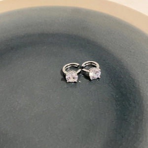 Dettaglio di orecchini a clip in argento con zirconi lucidi su vassoio in ceramica