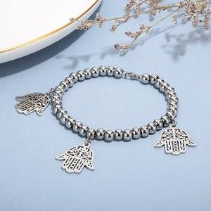 Silver bead stretch bracelet with Hamsa Hand pendants on a textured blue background