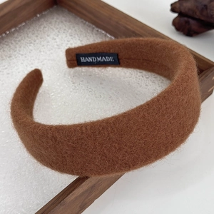 Close-up of brown plush fabric headband with a black handmade label on wooden tray