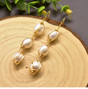 Macro shot of handmade wire-wrapped baroque pearl earrings on a natural wood base