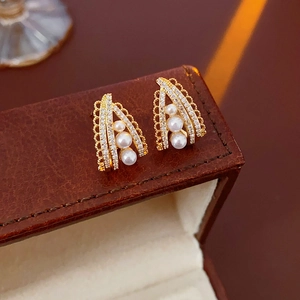 Macro view of gold pearl earrings featuring zircon stones in a vintage triangular frame