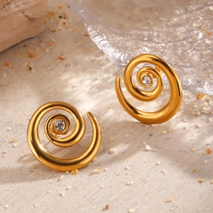 Minimalist gold spiral earrings with center crystal on natural wooden and glass background
