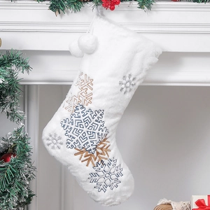 Plush white Christmas stocking with gold and silver snowflake embroidery on a warm fireplace