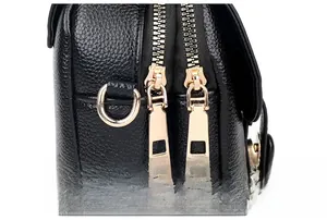 Detail of black lychee leather crossbody bag with dual polished gold zippers and D-ring