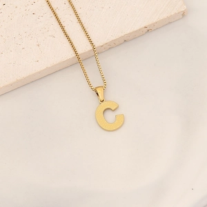 Macro view of gold letter C pendant with textured surface on a minimalist stone