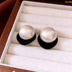 Close-up of elegant pearl and black velvet earrings displayed in a luxury wooden box