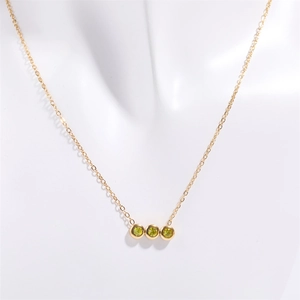 Détail d'un collier doré avec trois zircons verts sertis clos disposés horizontalement
