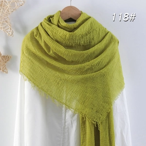 Détail d'une écharpe en coton vert moutarde avec texture froissée et franges sur cintre