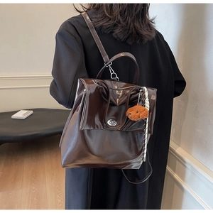 Detail of brown glossy leather backpack featuring a cute plush dog charm accessory