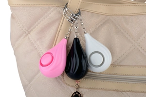 Three teardrop personal alarms in pink, black, and white hanging on a beige handbag