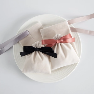Three creamy white velvet drawstring pouches with satin ribbon bows on a white plate