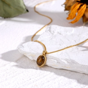 18k gold stainless steel necklace featuring an oval tiger eye stone on a stone slab