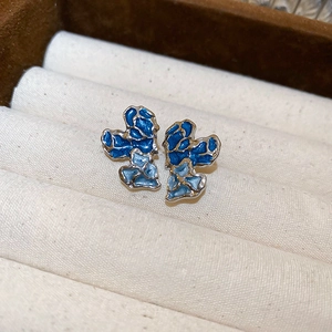 Macro view of vintage irregular flower studs with blue enamel on velvet padding