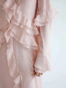 Detail of layered ruffles and flared sleeves on a powder pink chiffon dress texture
