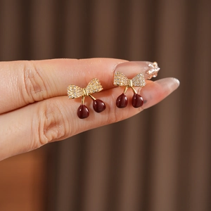 Vue macro de boucles d'oreilles cerise plaquées or avec nœuds en zircon et émail rouge