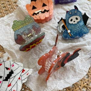 Close-up of glittery Halloween acrylic hair claws with pumpkin and ghost shapes