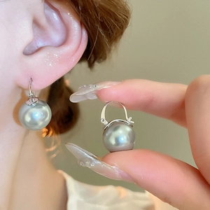 Détail d'une boucle d'oreille perle gris-bleu avec fermoir argenté sur une main