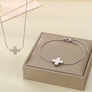 Detail of silver cross pendant necklace and adjustable bracelet set on beige gift box