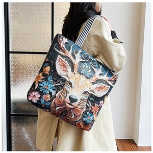 Black canvas tote bag with colorful deer embroidery and striped shoulder strap in use