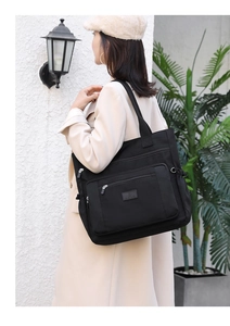 Détail d'un sac à épaule noir en nylon avec fermetures éclair porté avec un manteau beige
